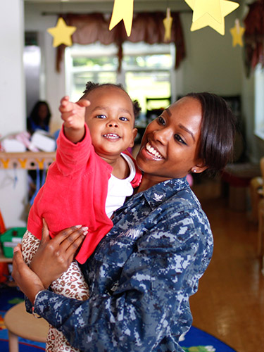 A woman holds a smiling toddler as he reaches for a star hanging from a mobile