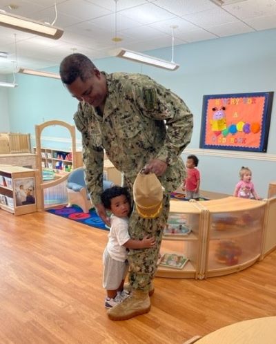 Navy father in uniform with young child hugging his leg at Child Development Center